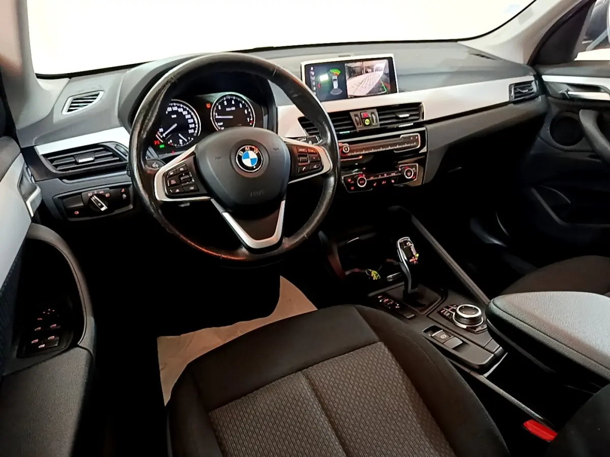 Vue intérieure côté conducteur du BMW X1 2020 noir, avec volant cuir multifonctions et écran tactile 8,8 pouces allumé.