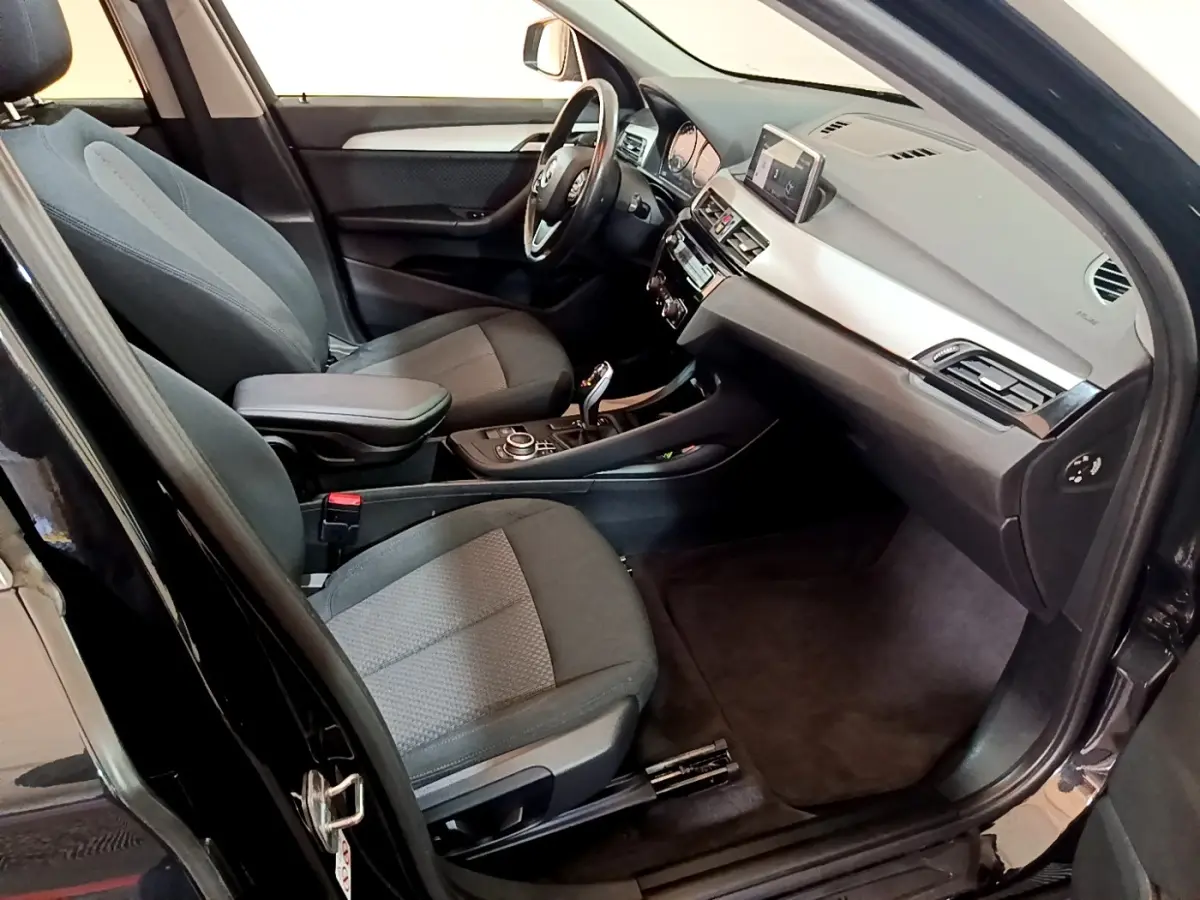Intérieur côté conducteur d’un BMW X1 noir 2020, montrant sièges tissu gris et tableau de bord avec écran tactile.