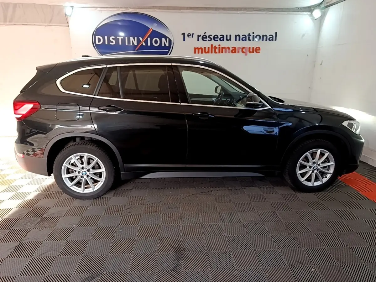 BMW X1 sDrive20i noir vue de profil côté gauche dans un showroom avec logo Distinxion en arrière-plan.