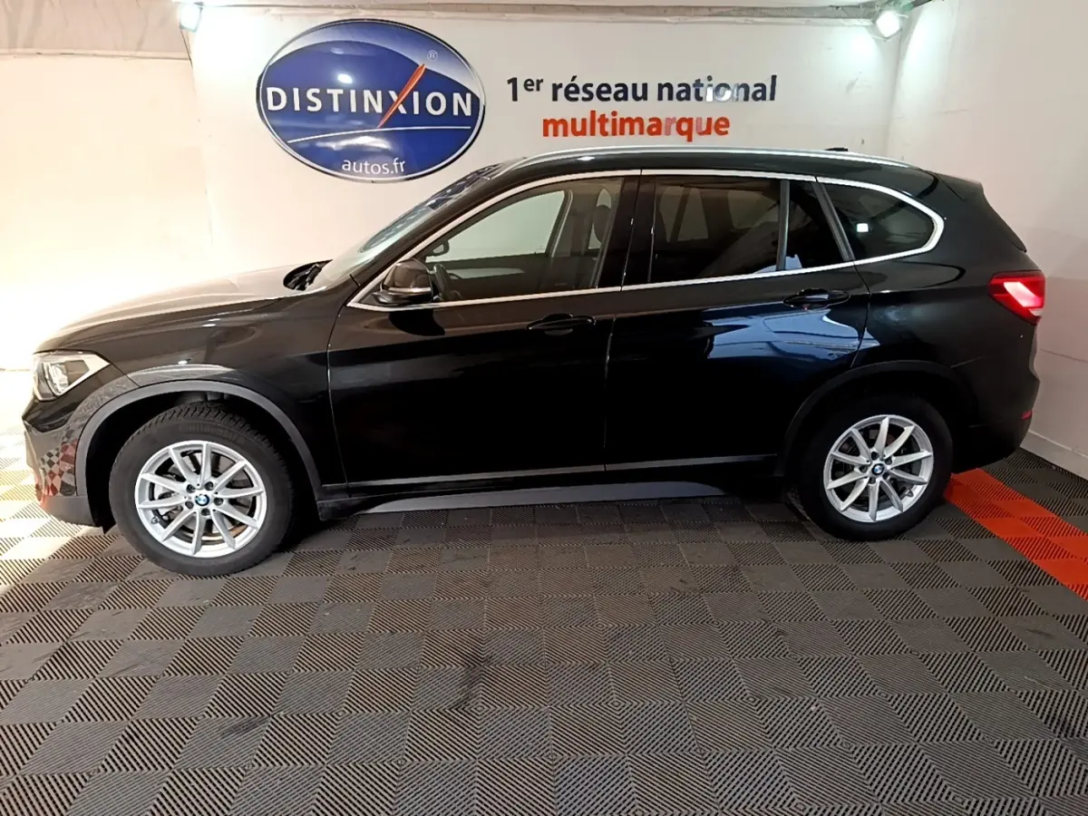 BMW X1 sDrive20i noir vue de profil côté gauche, stationné en intérieur avec logo Distinxion en arrière-plan.