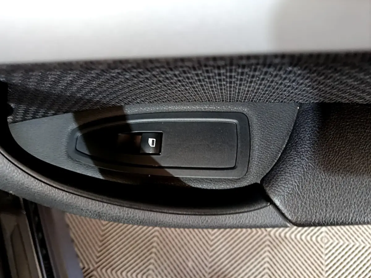Gros plan sur le bouton de commande de la vitre électrique côté conducteur d'un BMW X1 noir.
