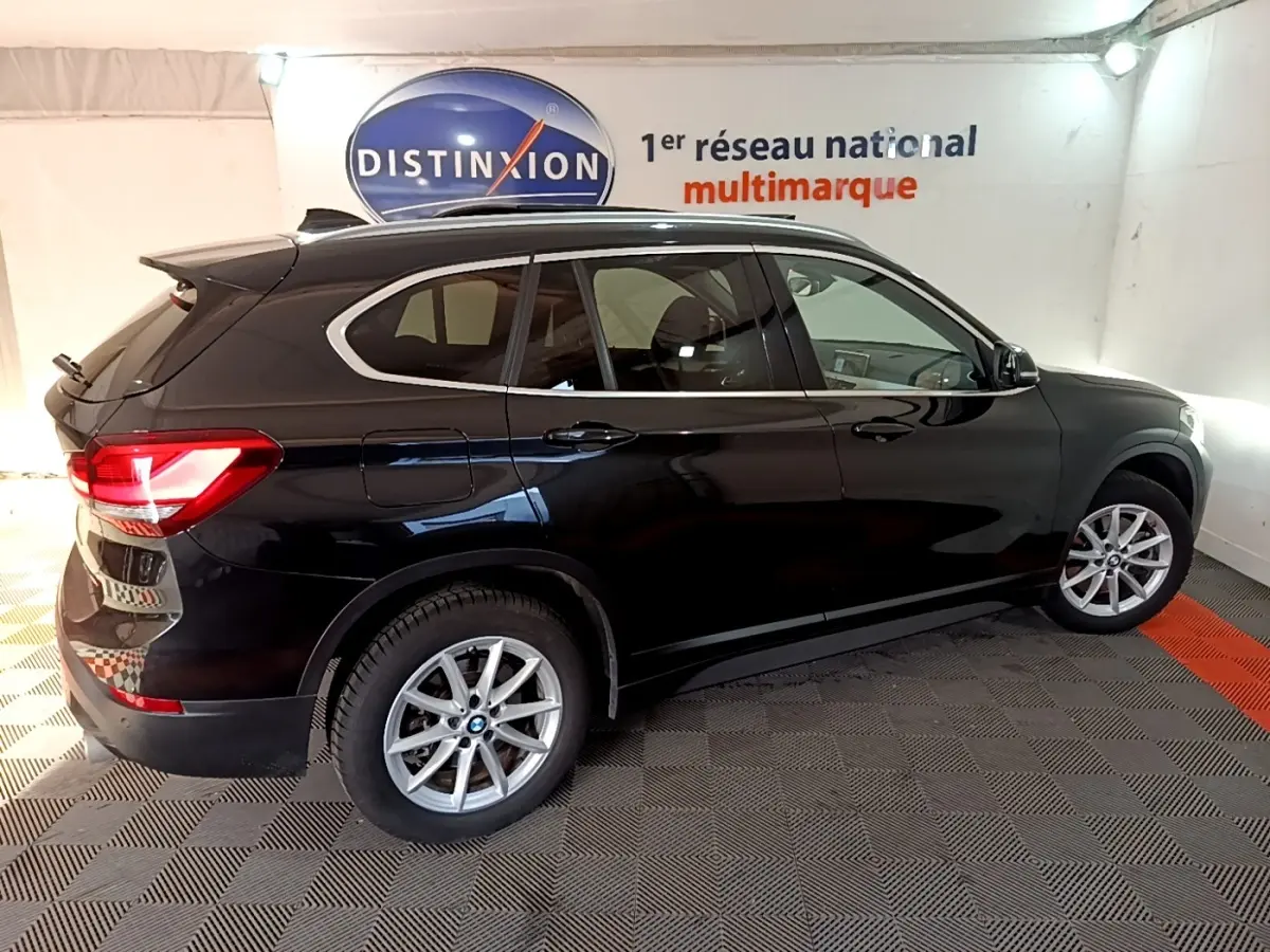 BMW X1 noir vue de profil côté droit dans un showroom avec jantes alliage et feux arrière allumés.