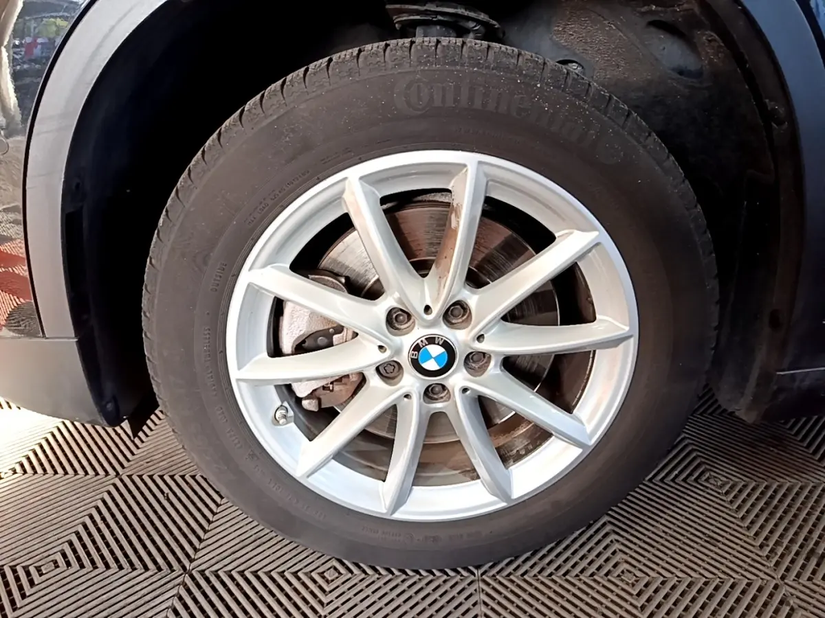 Gros plan sur la roue avant gauche d’un BMW X1 noir, mettant en valeur la jante argentée à 10 branches.