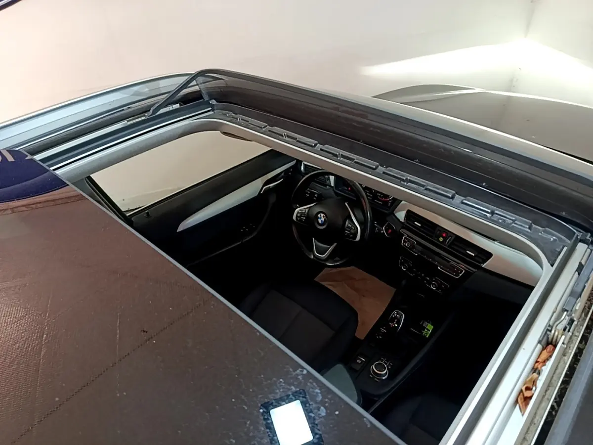 Vue plongeante sur l'intérieur noir d'une BMW X1 sDrive20i 2020 avec toit ouvrant panoramique partiellement ouvert.