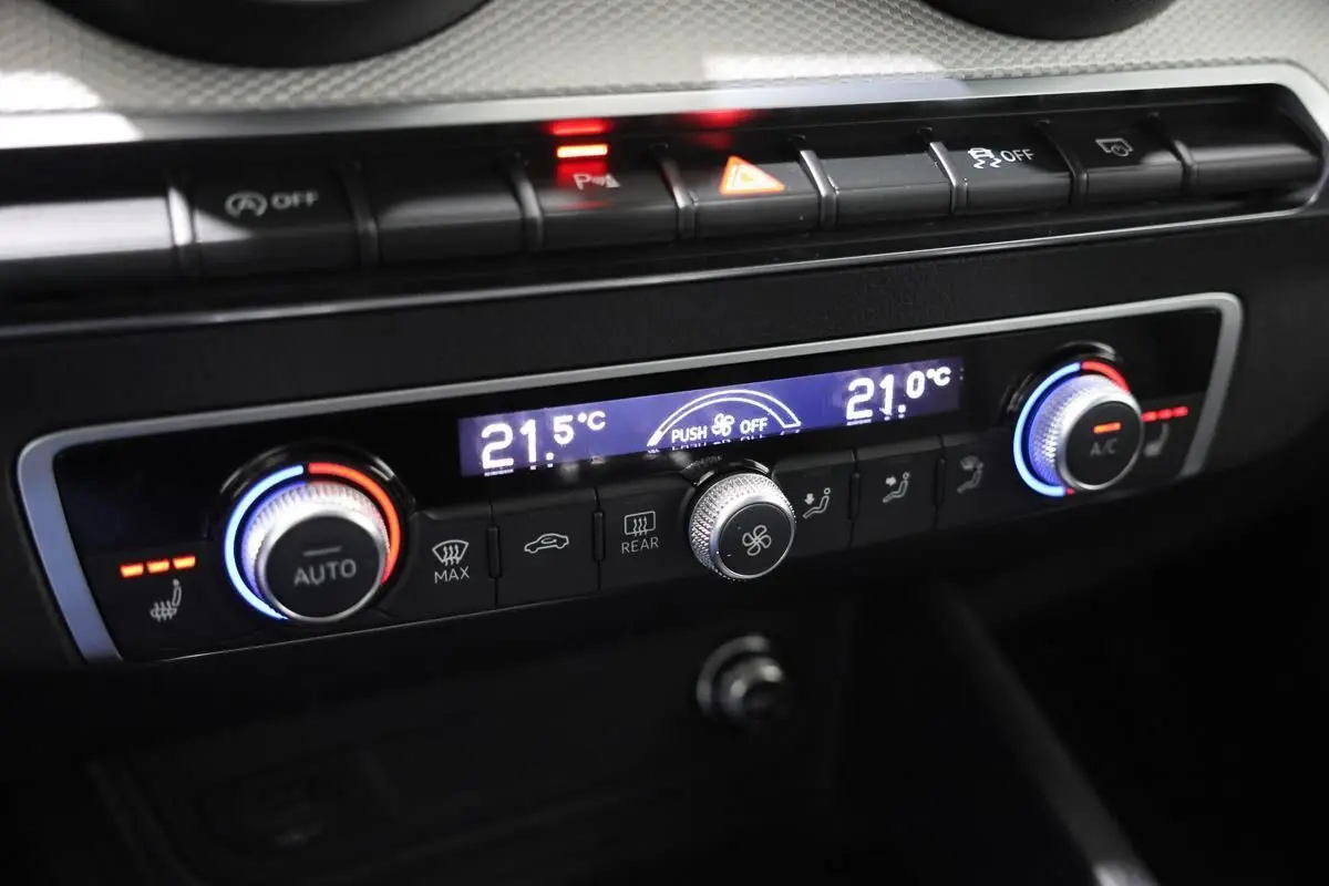 Gros plan sur la console de climatisation de l’Audi Q2 gris, avec réglages digitaux et boutons rétroéclairés.