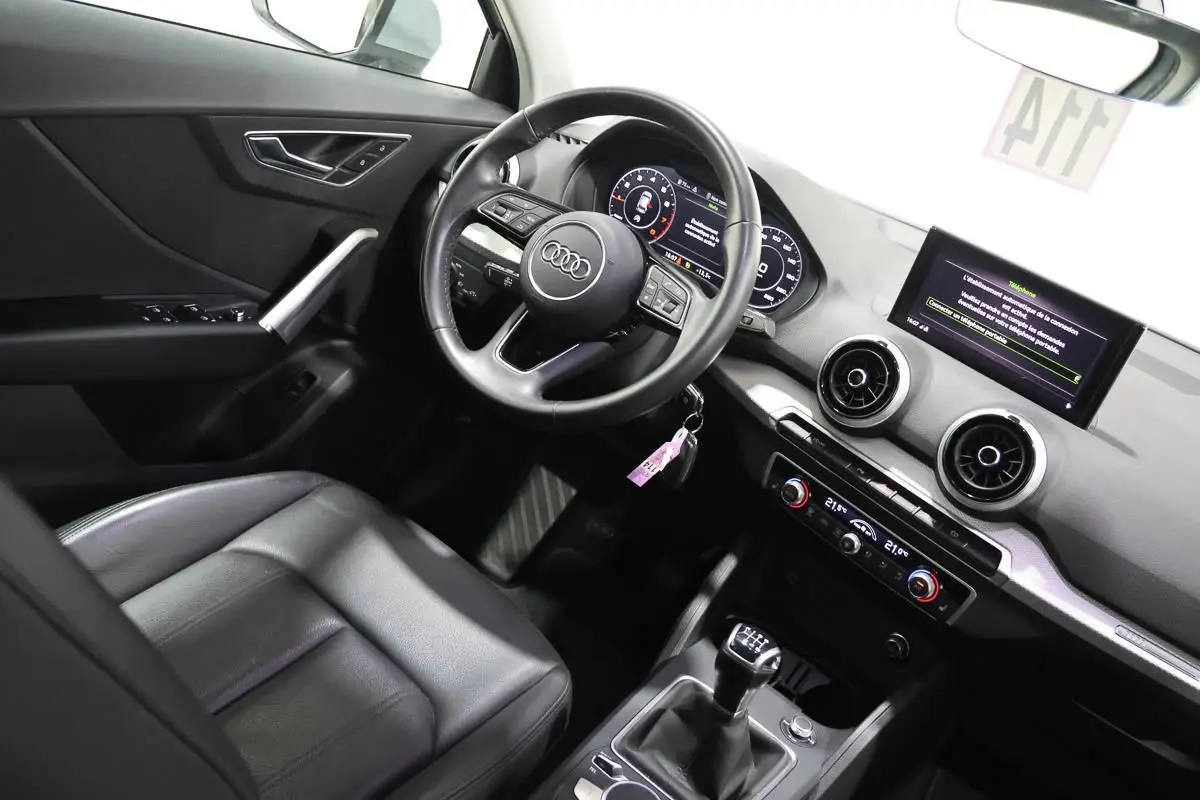 Vue intérieure côté conducteur de l'Audi Q2 gris, volant cuir, écran digital et sièges cuir chauffants visibles.