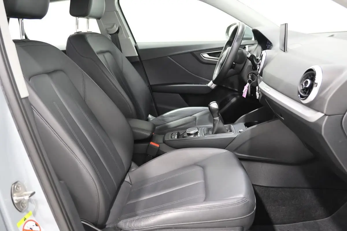 Vue intérieure côté conducteur de l'Audi Q2 2023, sièges cuir noirs et tableau de bord avec écran GPS escamotable.