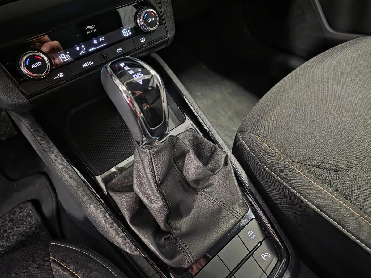 Gros plan sur le levier de vitesses automatique noir et la console centrale du Skoda Kamiq gris, avec commandes de climatisation visibles.