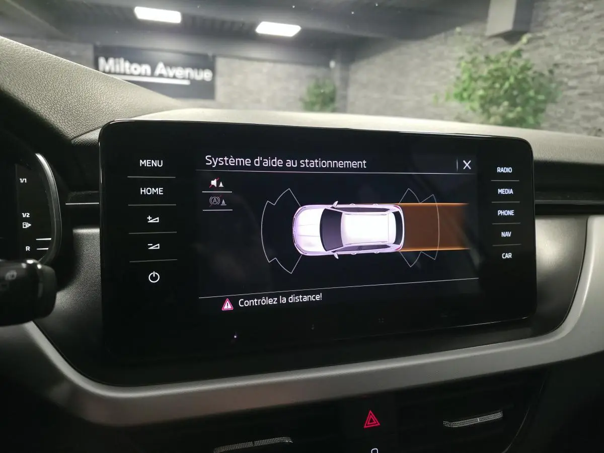 Écran tactile intérieur du Skoda Kamiq 2023 montrant l'aide au stationnement avec vue du véhicule en blanc.