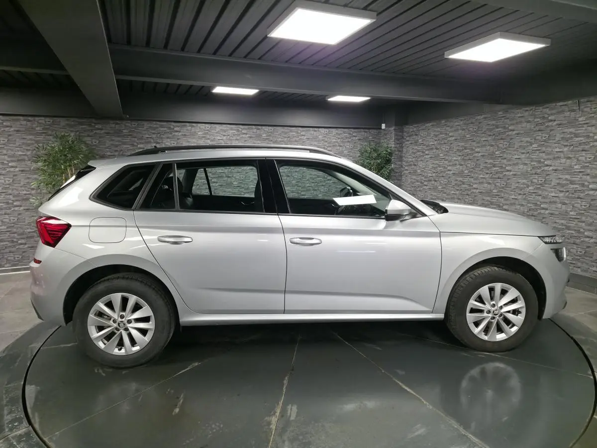 Vue de profil côté gauche d'un Skoda Kamiq gris métallisé 2023, avec jantes alliage et barres de toit noires.