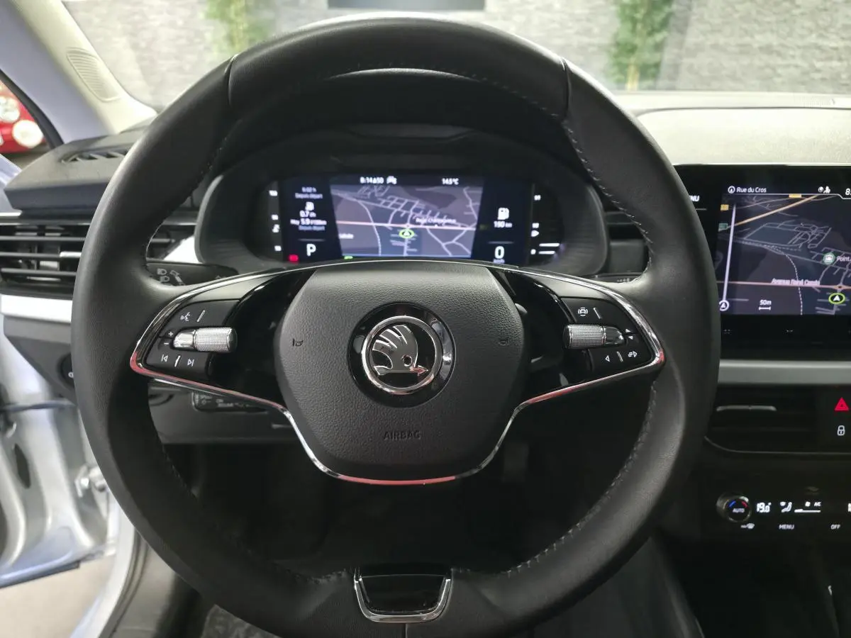 Vue rapprochée du volant cuir noir de la Skoda Kamiq 2023 avec tableau de bord digital et écran de navigation allumé.