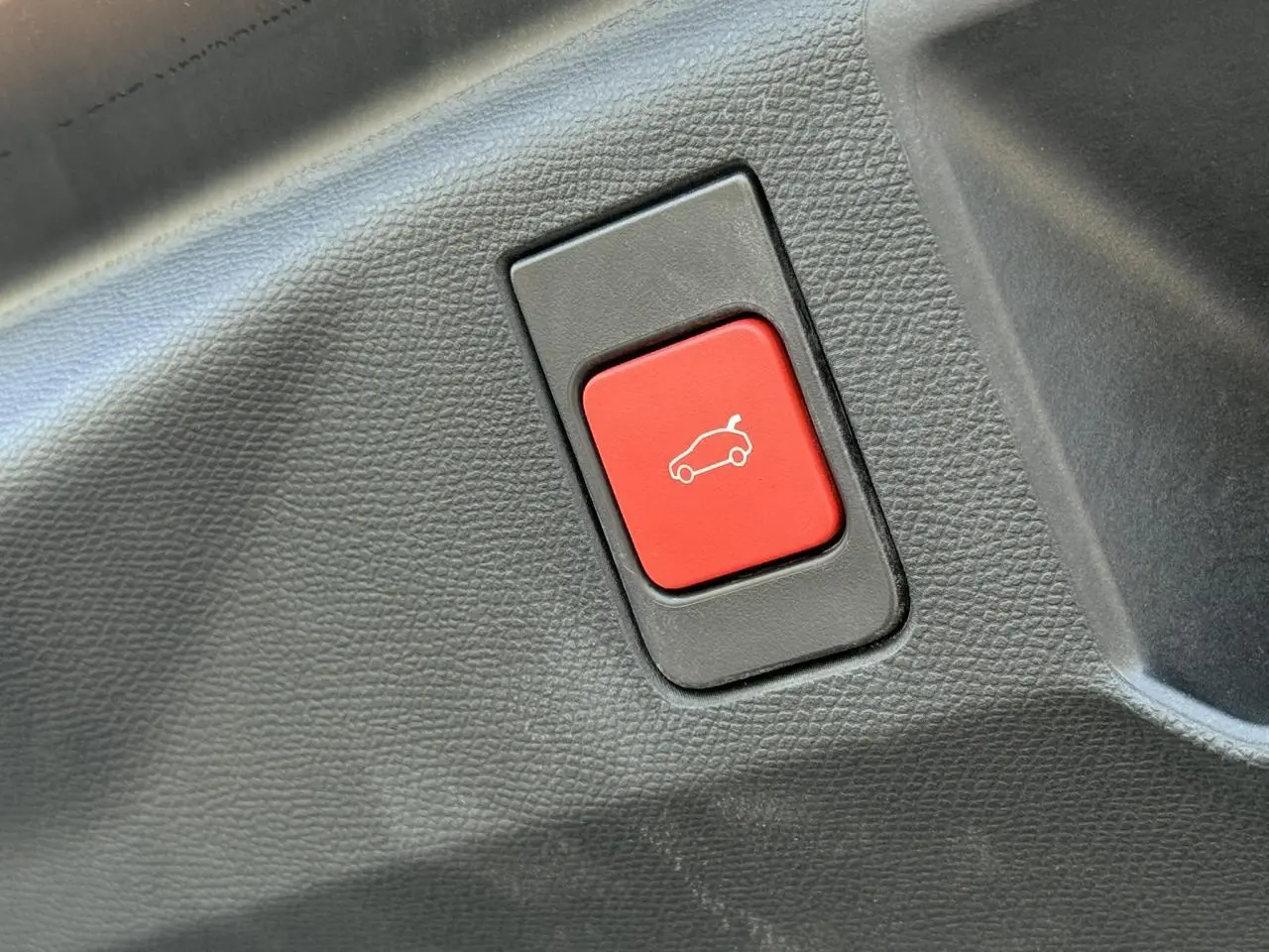 Gros plan sur le bouton rouge d'ouverture électrique du hayon dans l'habitacle du Peugeot 5008 noir Perla.