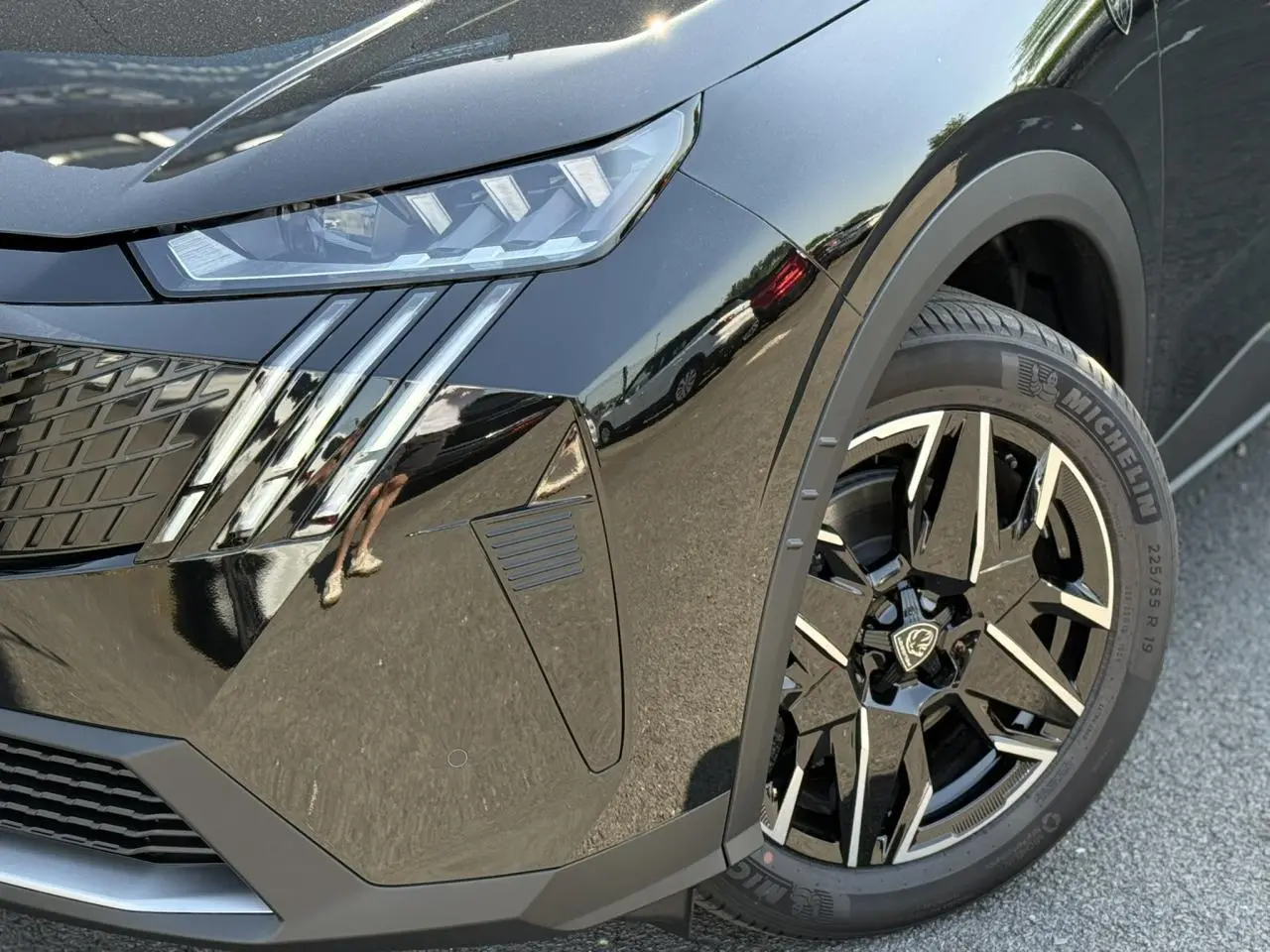 Gros plan sur l'avant droit noir Perla du Peugeot 5008 Hybrid 145 GT, mettant en valeur le phare LED et la jante alliage 19 pouces.