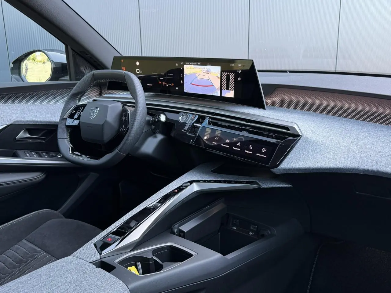 Vue intérieure côté conducteur du Peugeot 5008 Hybrid 2026, mettant en valeur le tableau de bord moderne avec écran incurvé et sellerie Alcantara grise.