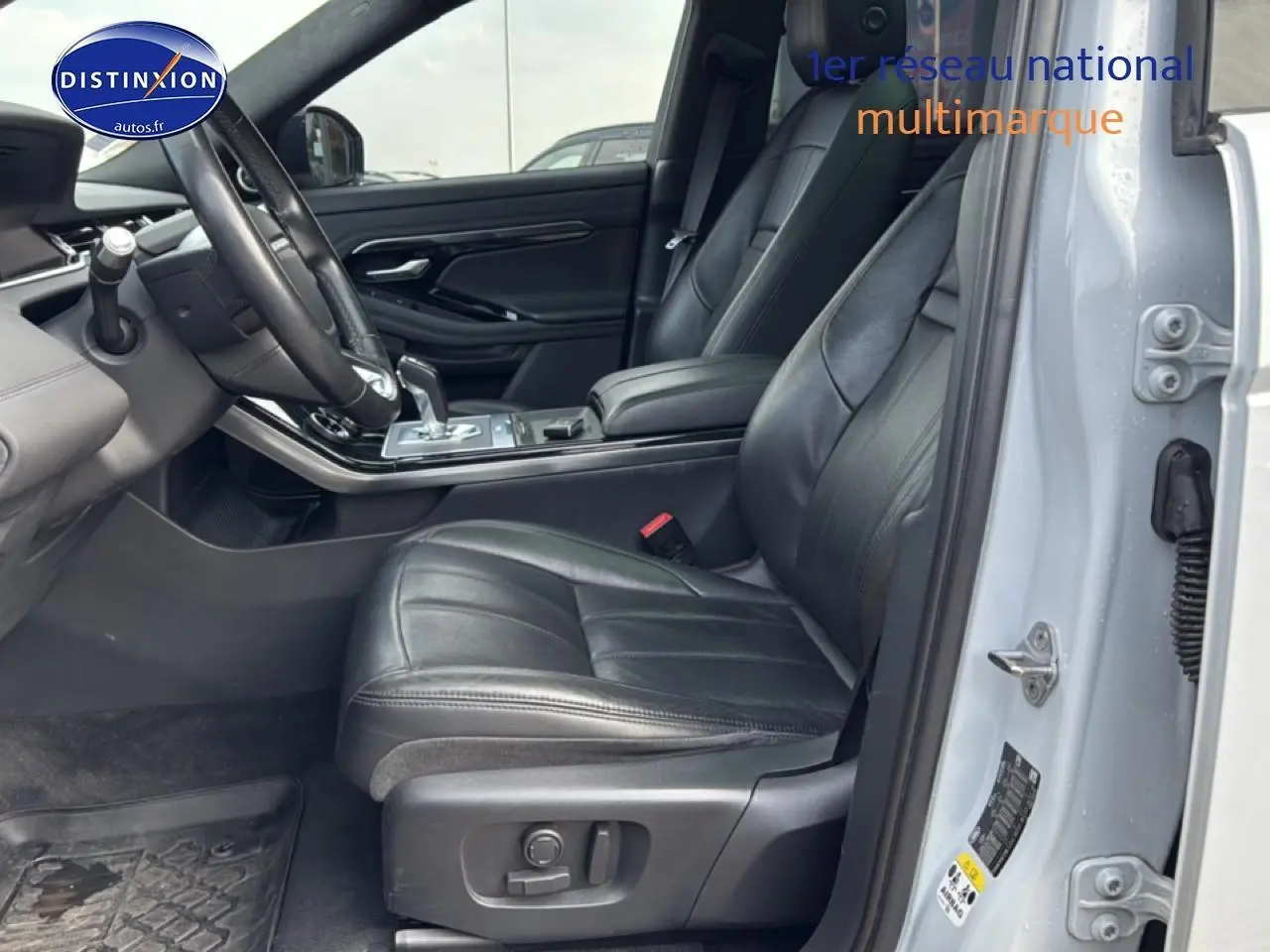 Vue intérieure côté conducteur du Range Rover Evoque blanc, mettant en valeur les sièges cuir noirs et l'accoudoir central.