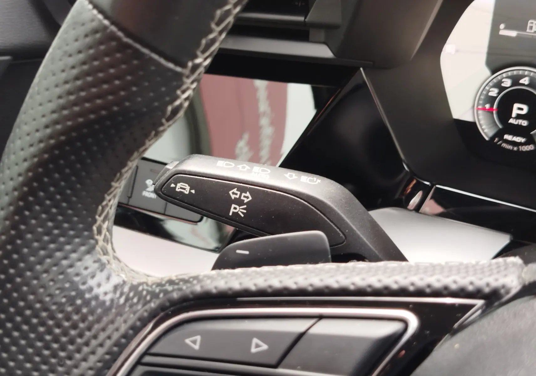 Gros plan sur le commodo de clignotant noir et le volant perforé de l'Audi A3 Sportback blanc Glacier 2022, intérieur moderne.