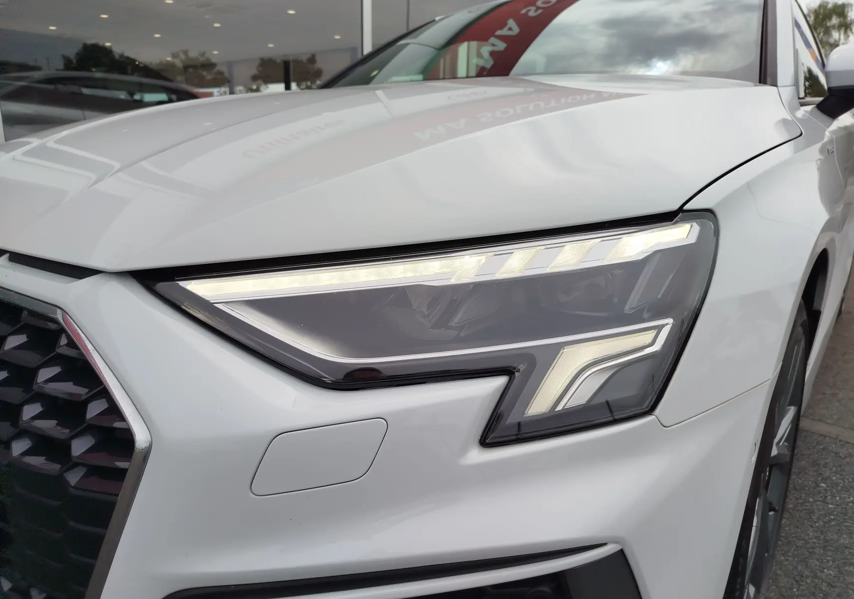 Gros plan sur le phare avant droit blanc glacier métallisé de l'Audi A3 Sportback 30 TFSI S line 2022.