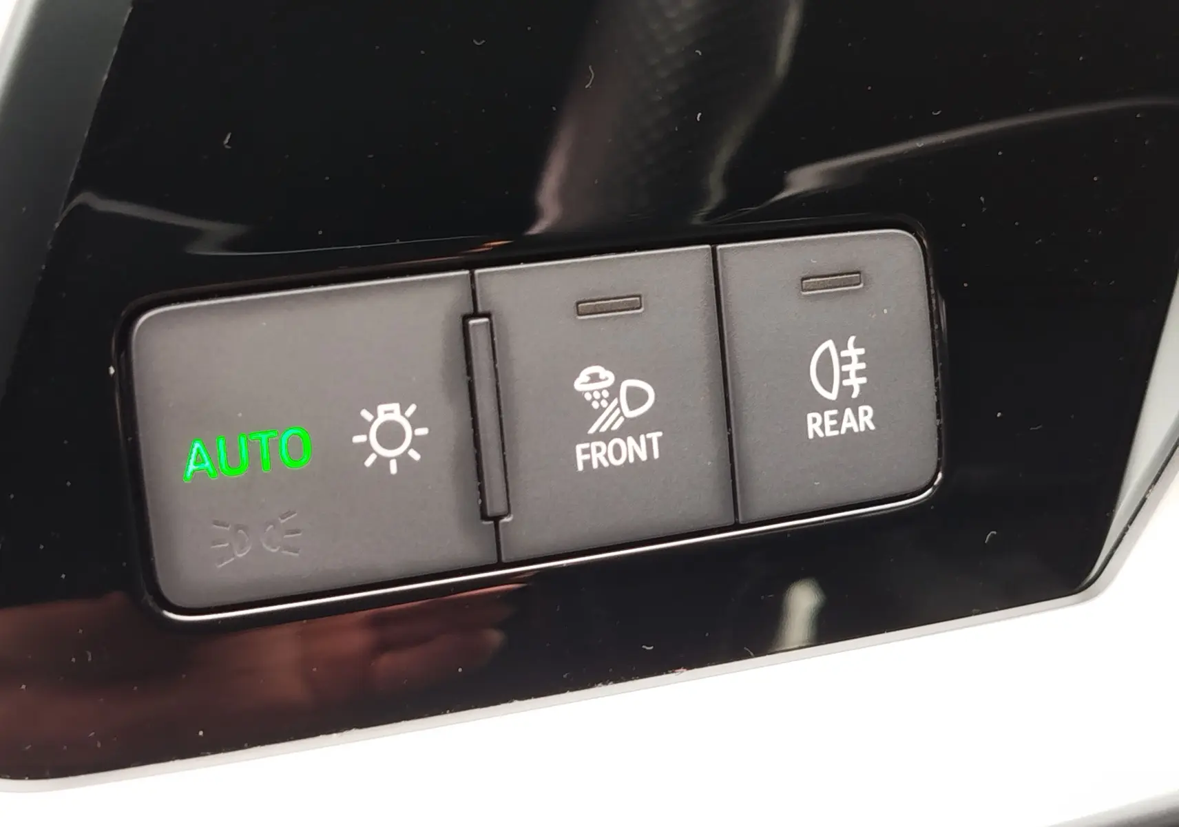 Gros plan sur les boutons de commande des feux avec indication "AUTO" verte dans l'Audi A3 Sportback blanc Glacier.