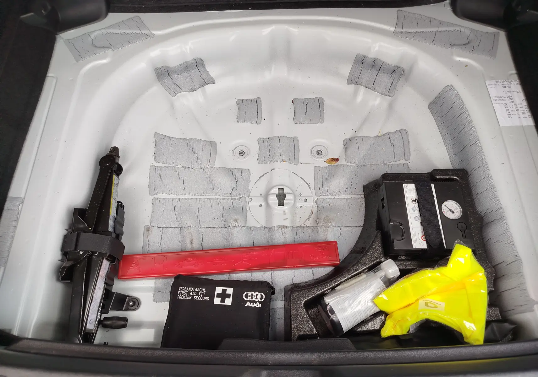 Vue plongeante sur le coffre blanc glacier métallisé d'une Audi A3 Sportback 2022, montrant le rangement d'outils et kit de secours.