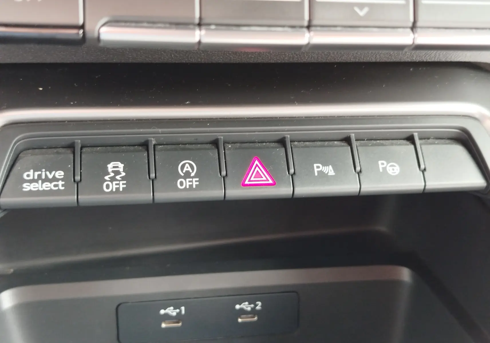 Gros plan sur la rangée de boutons de commande noirs avec témoin rouge d'alerte allumé dans l'Audi A3 Sportback blanc Glacier.