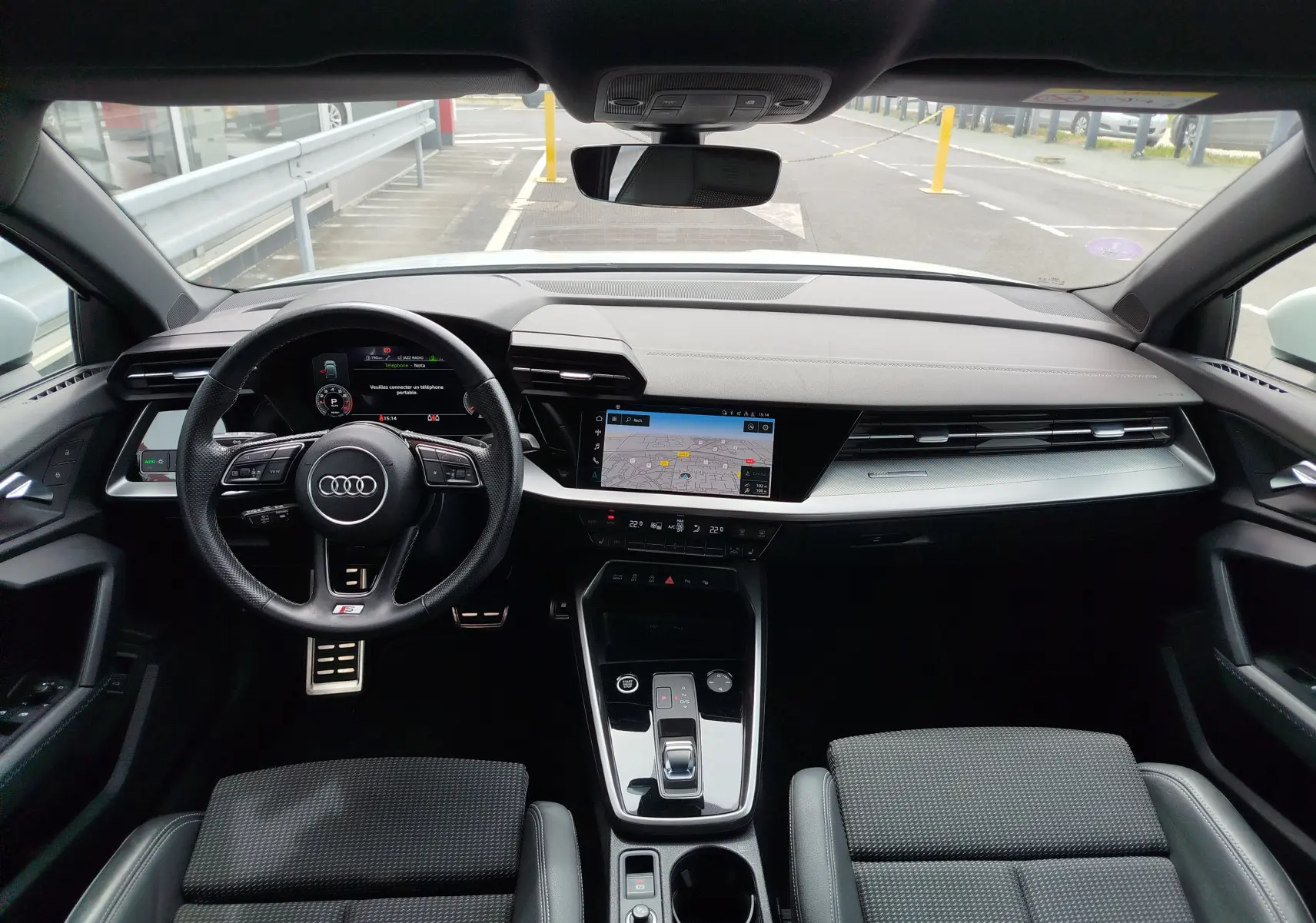 Vue intérieure avant de l'Audi A3 Sportback 2022, tableau de bord moderne avec écran tactile et volant multifonction noir.