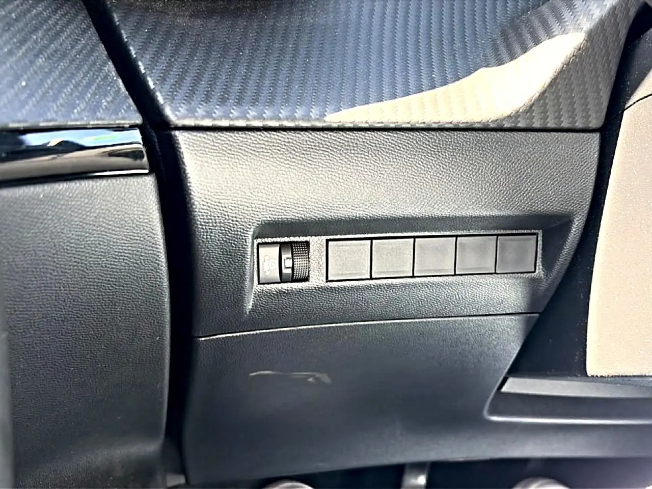 Détail intérieur côté conducteur du tableau de bord noir avec commande de réglage de phares sur Peugeot 2008 gris 2025.