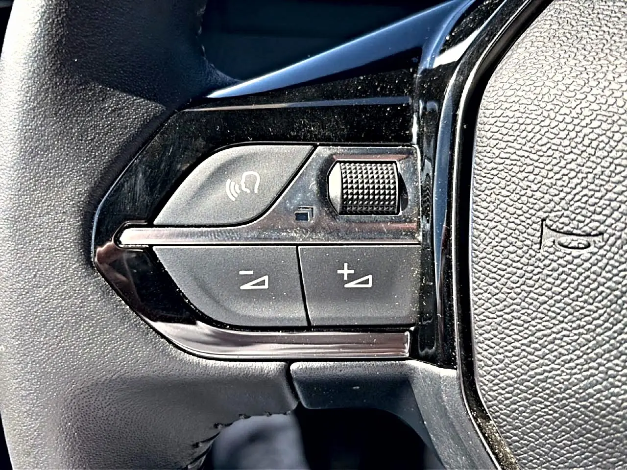 Gros plan sur les commandes de volume et appel mains-libres sur le volant noir du Peugeot 2008 gris.