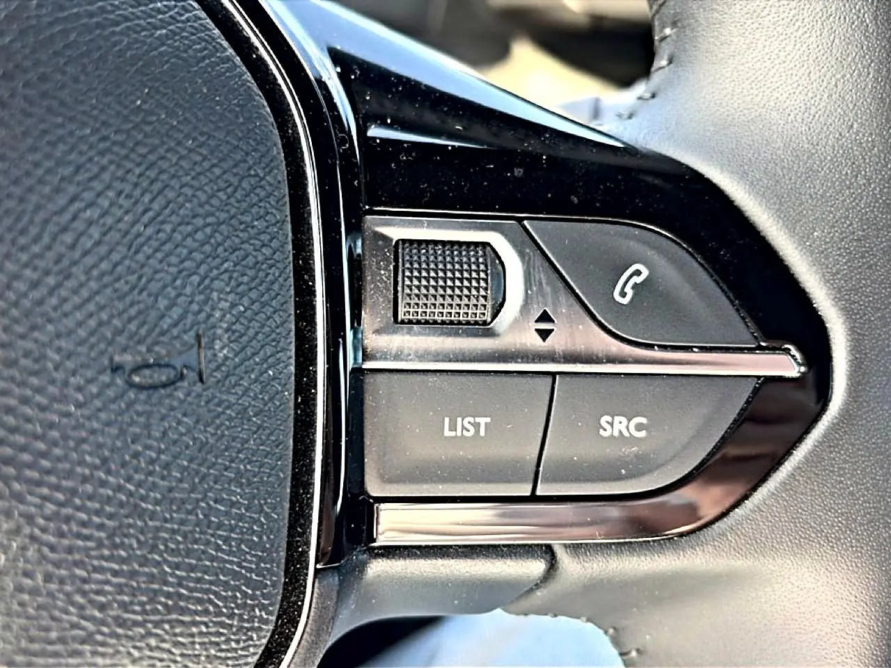 Gros plan sur les commandes gauche du volant noir du Peugeot 2008 gris, avec boutons multifonctions et molette.