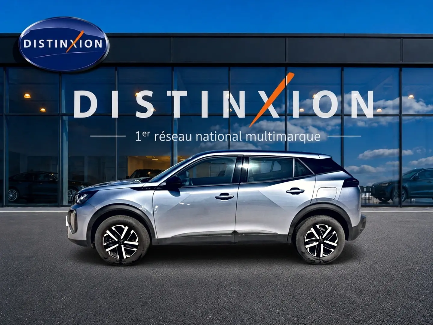 Peugeot 2008 gris en profil droit, avec toit noir et jantes noires à motifs blancs, devant une vitrine Distinxion.