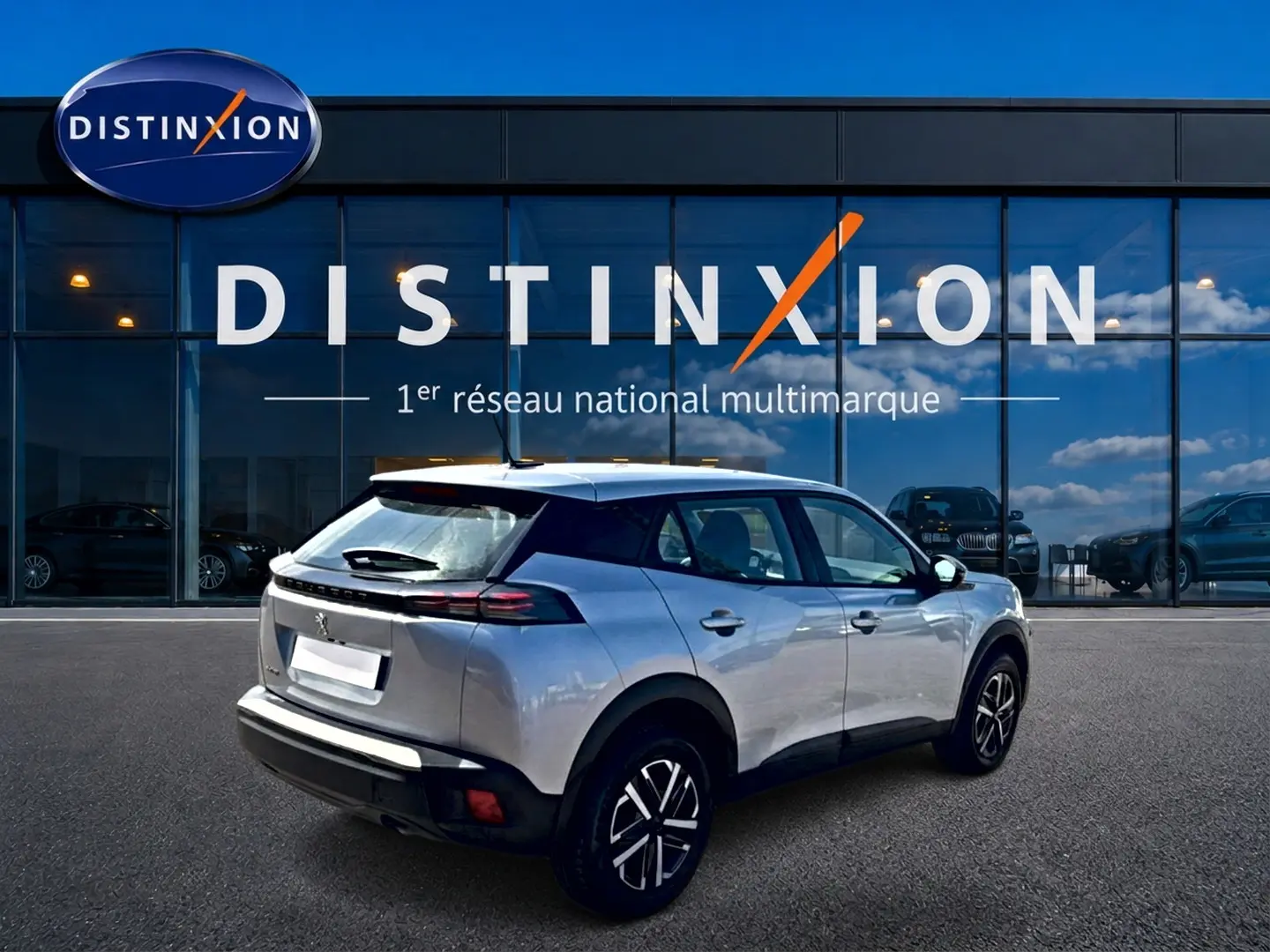 Peugeot 2008 gris en 3/4 arrière droit, avec becquet et feux arrière LED, devant un showroom Distinxion.