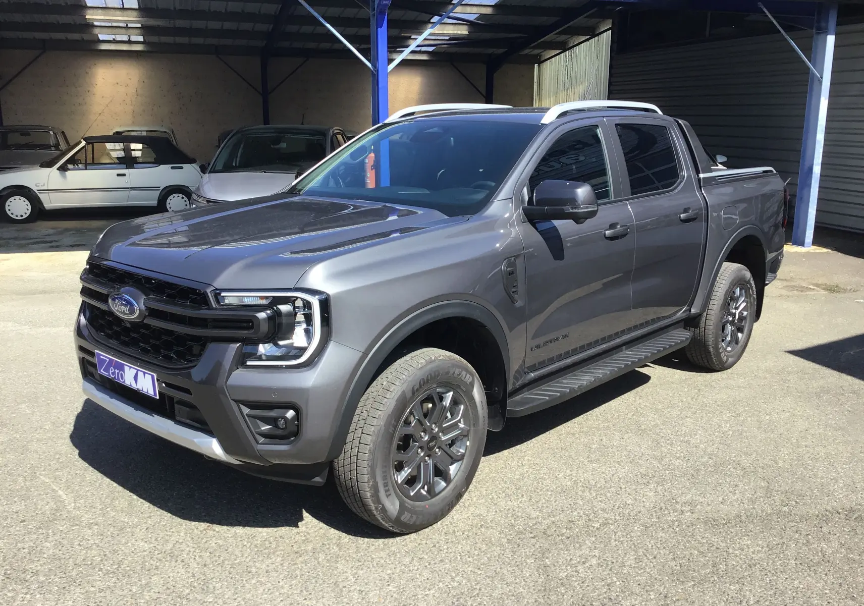Ford Ranger Double Cabine gris carbone vu en 3/4 avant droit avec marchepied et jantes alliage sombres.