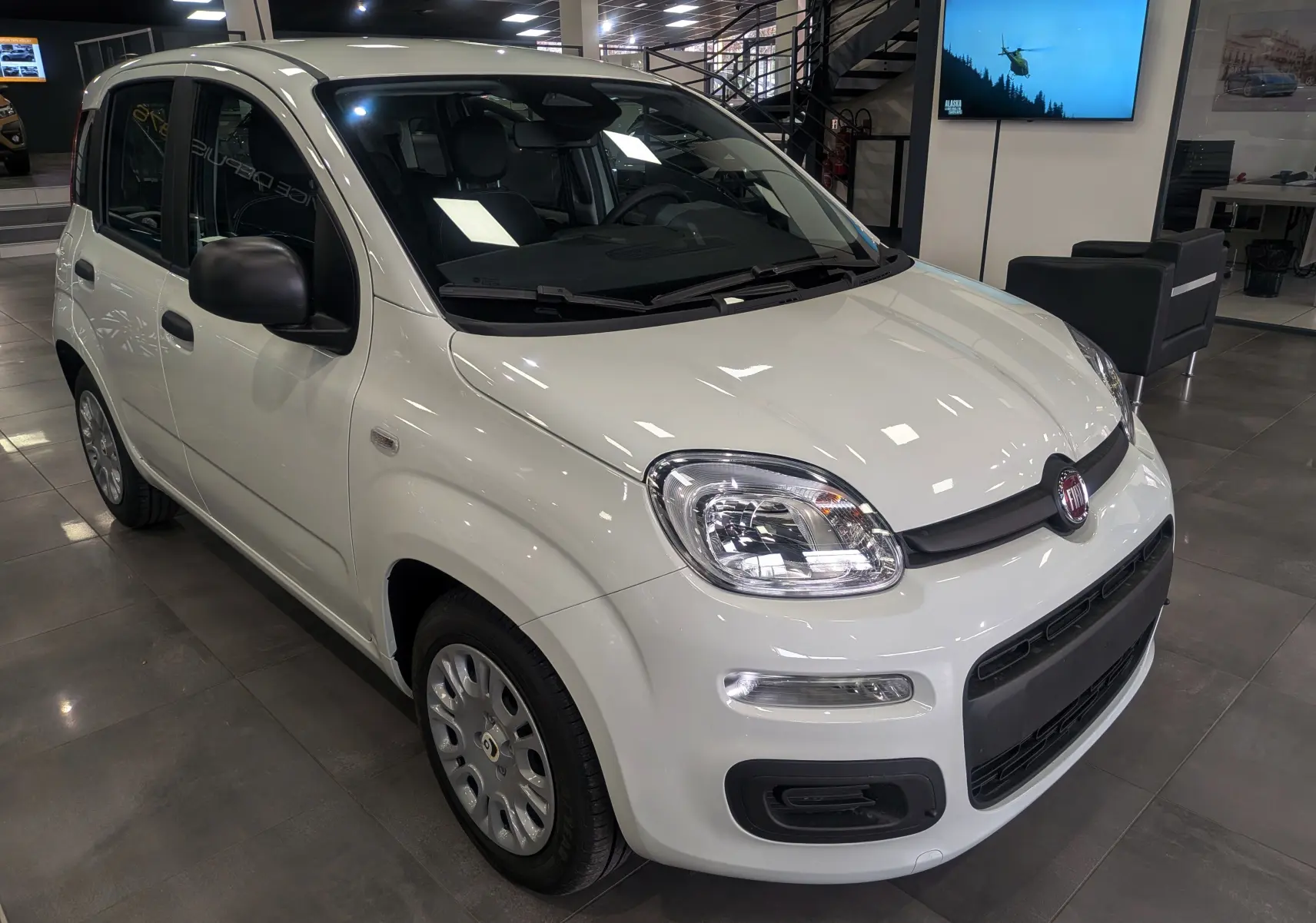 Vue 3/4 avant d'une Fiat Panda 1.0 70 CH Hybrid City blanche Gelato en showroom, avec rétroviseurs noirs et jantes acier.
