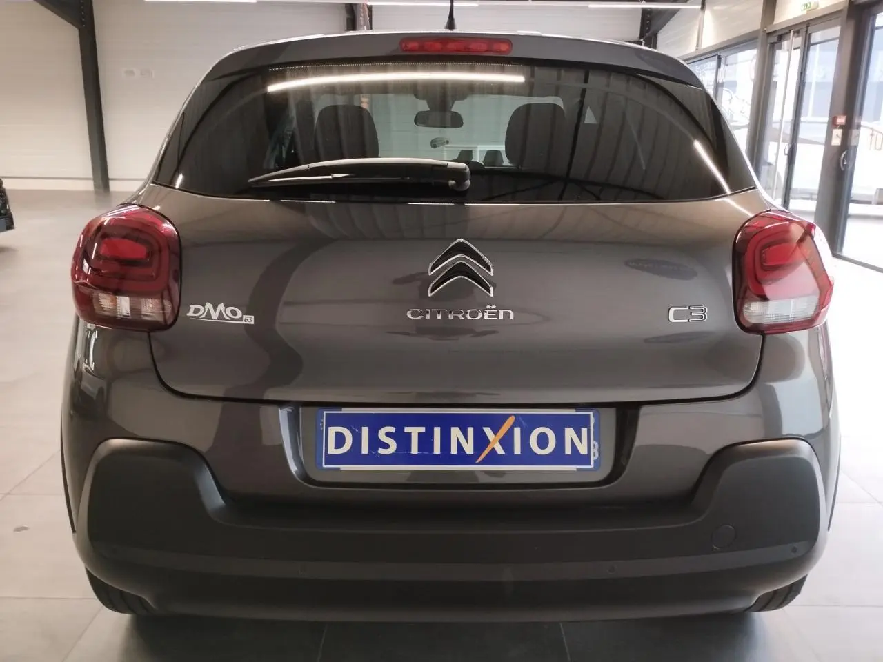 Vue arrière d'une Citroën C3 gris foncé 2024 avec feux arrière arrondis et pare-chocs noir mat en intérieur showroom.