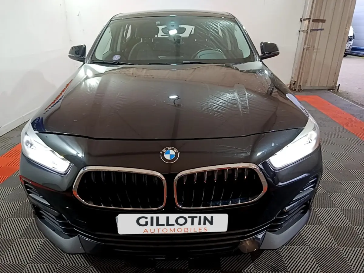 Vue avant d'un BMW X2 sDrive18i Lounge noir avec phares LED allumés dans un garage.
