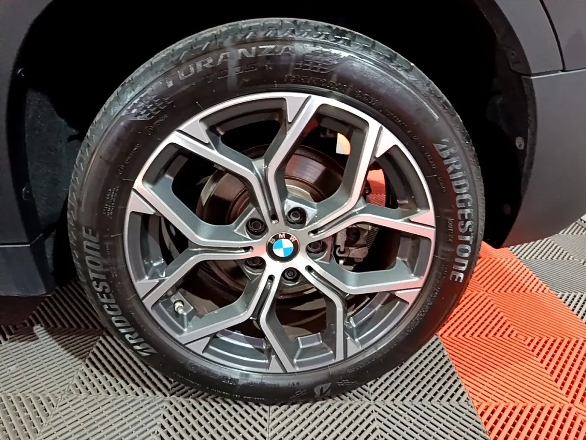 Gros plan sur la roue avant droite d’un BMW X2 noir avec jante alliage à design moderne et logo BMW central.