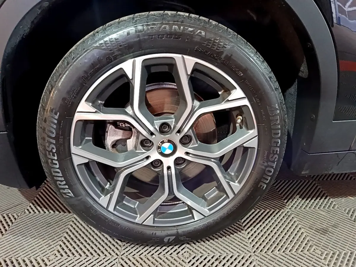 Gros plan sur la roue avant droite d’une BMW X2 noire avec jante alliage et pneu Bridgestone Turanza.