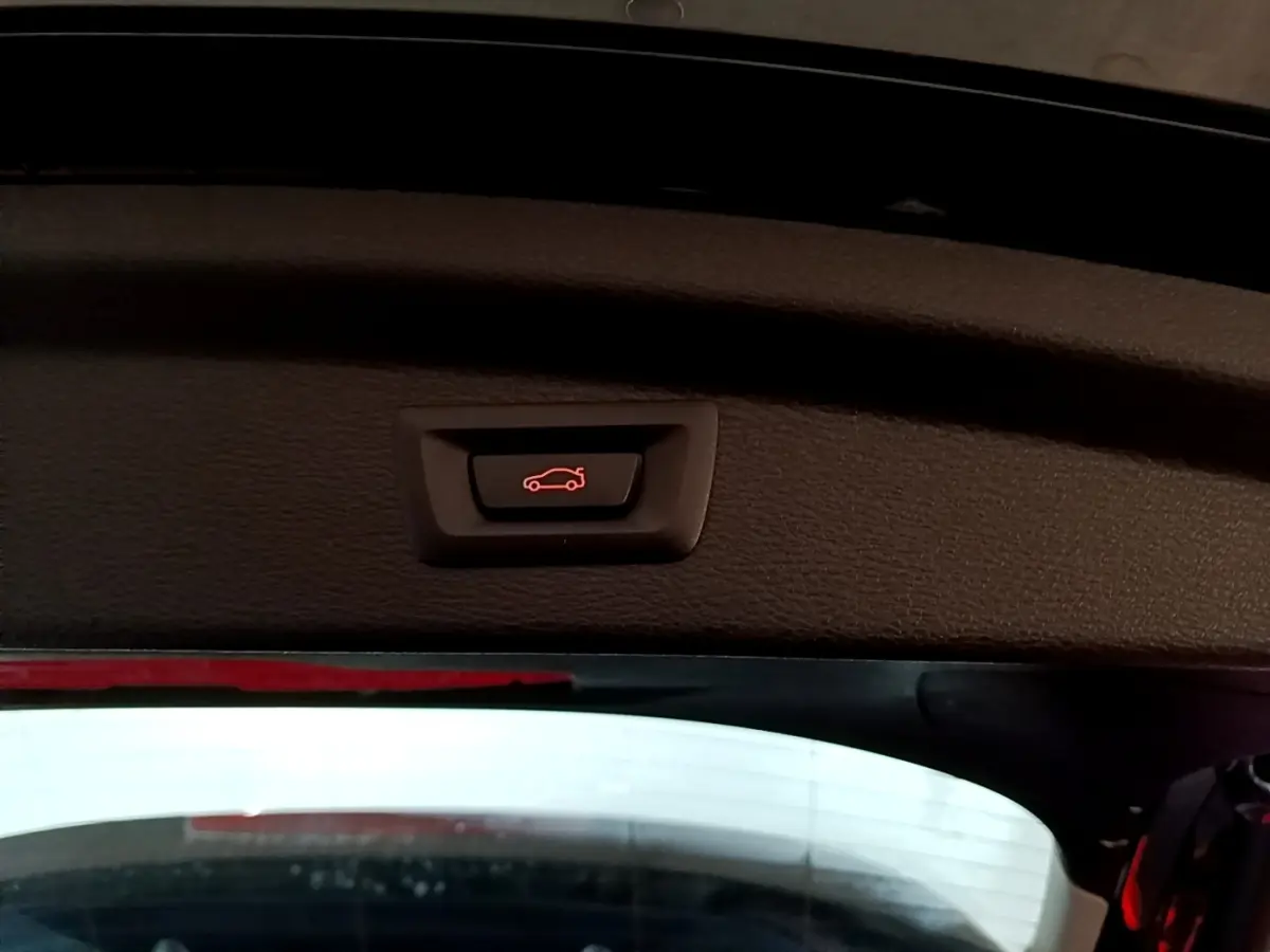 Bouton d'ouverture électrique du coffre visible sur la partie intérieure du hayon d'une BMW X2 noire.
