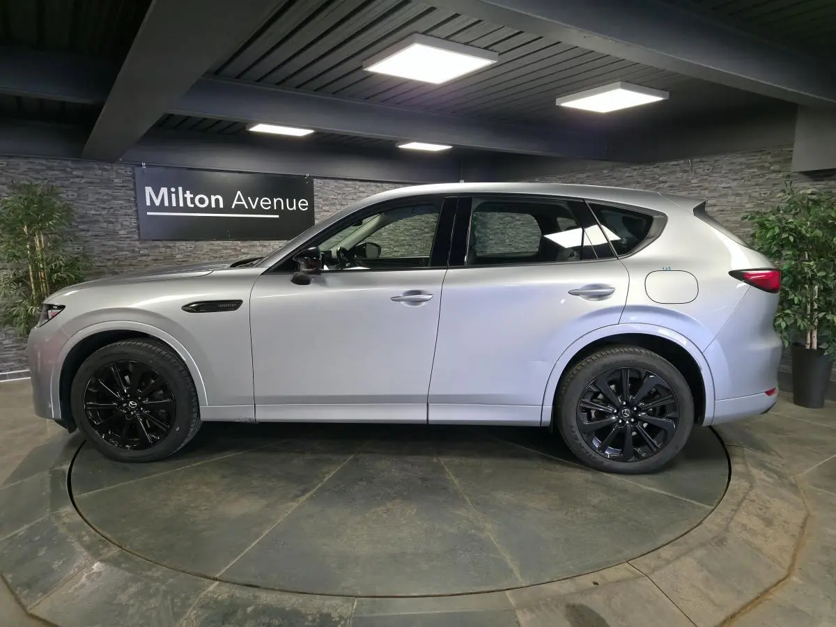 Vue latérale droite du Mazda CX-60 gris Sonic Silver avec jantes alliage noires dans un showroom intérieur.