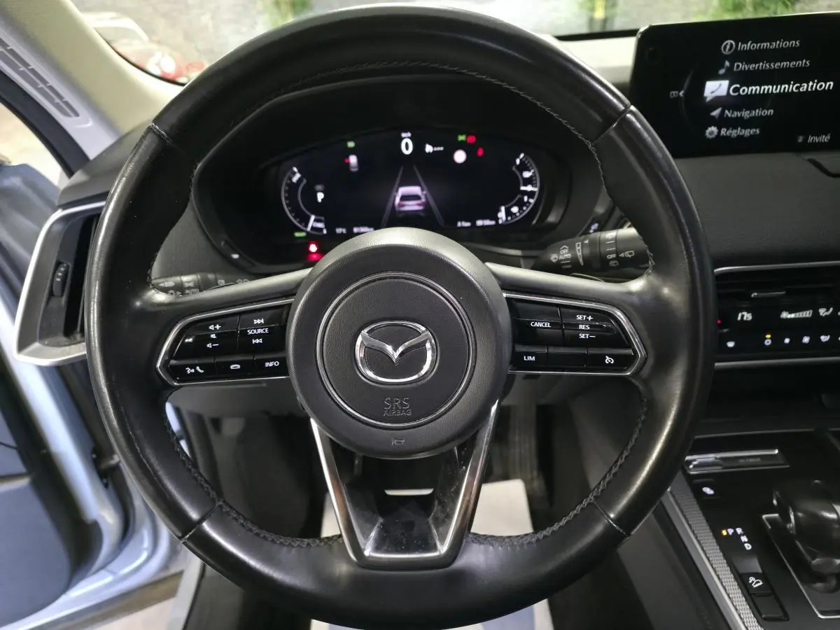 Vue frontale du volant cuir noir du Mazda CX-60 gris avec commandes intégrées et tableau de bord numérique allumé.