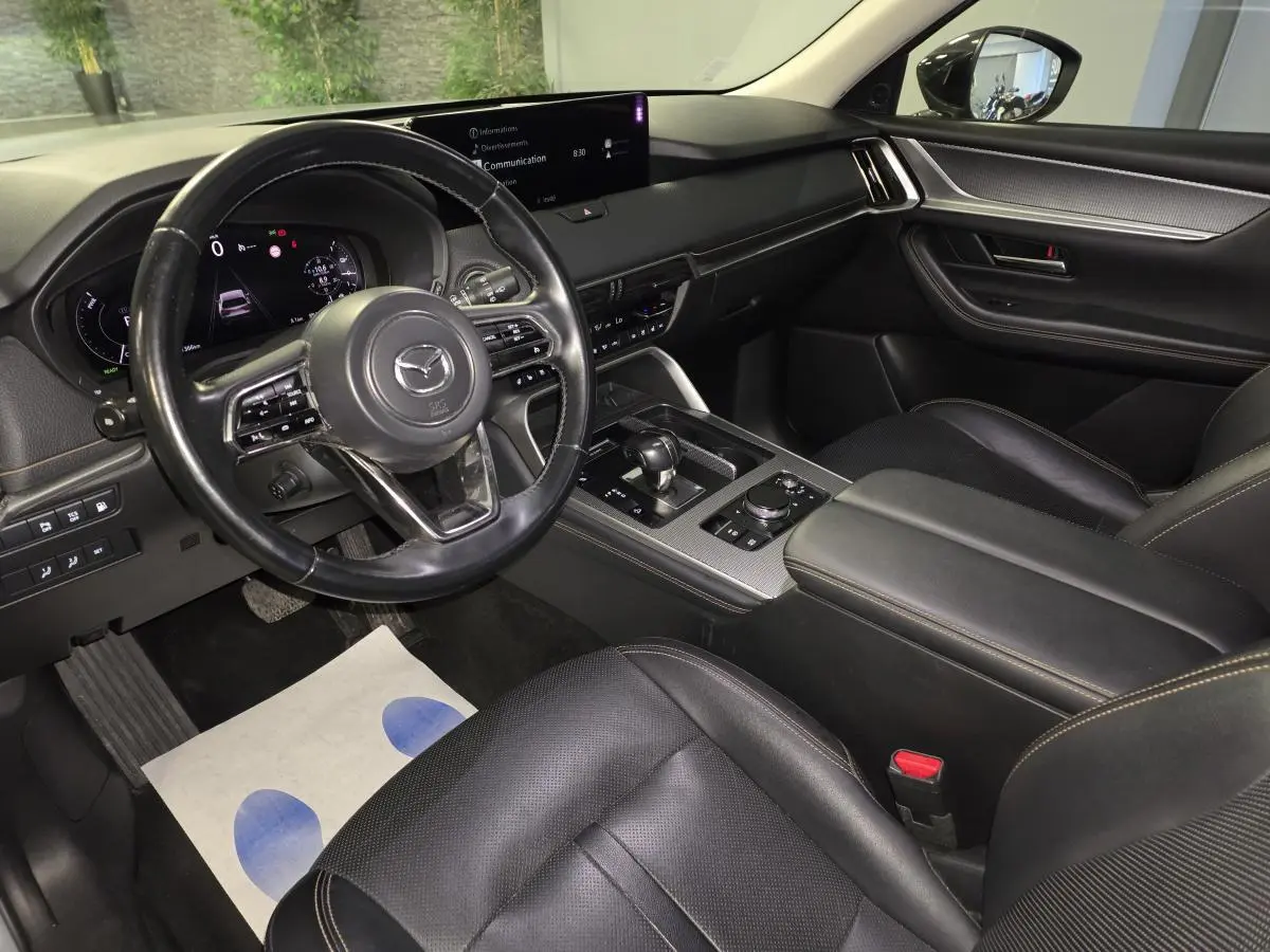 Intérieur avant du Mazda CX-60 gris, vue côté conducteur, volant cuir noir et console centrale avec écran tactile.