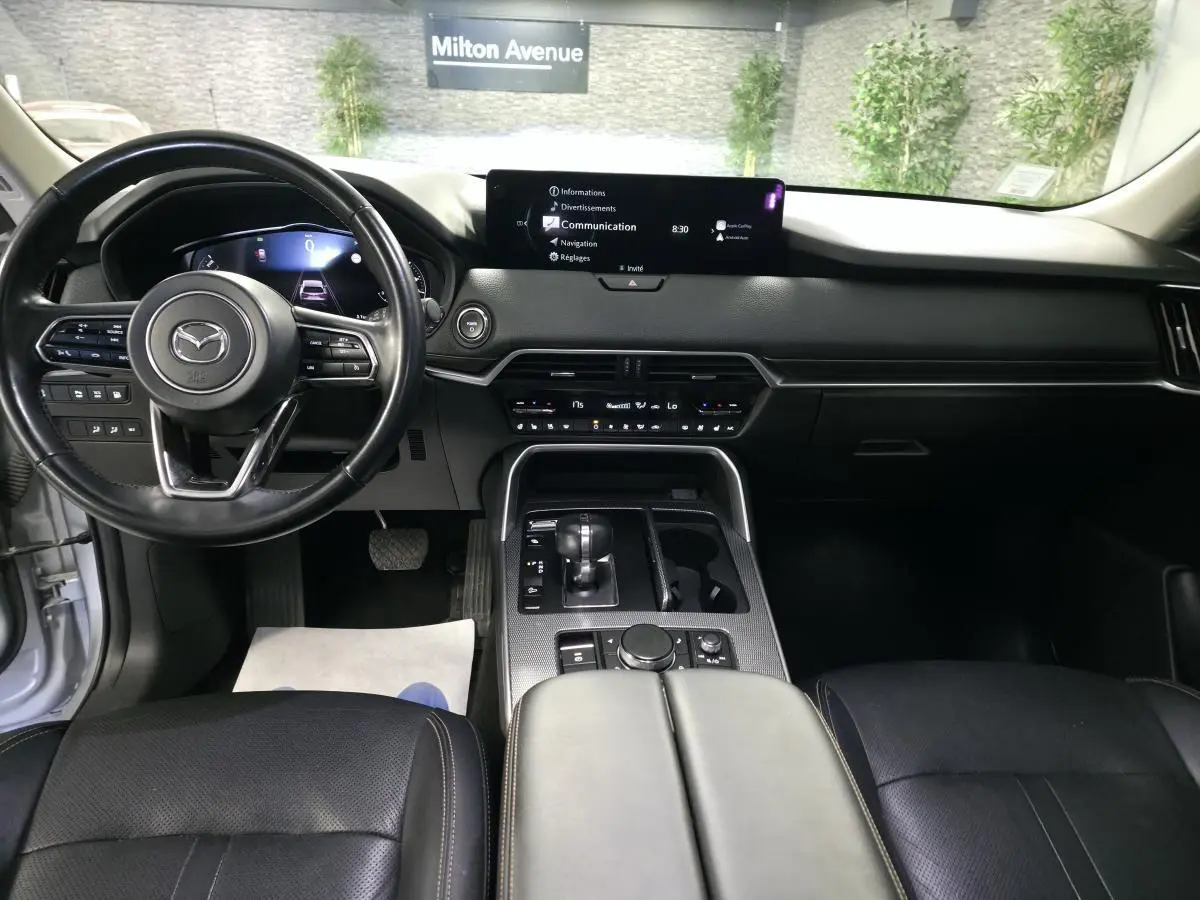 Vue intérieure avant du Mazda CX-60 gris, tableau de bord noir avec écran central large et volant cuir multifonction.