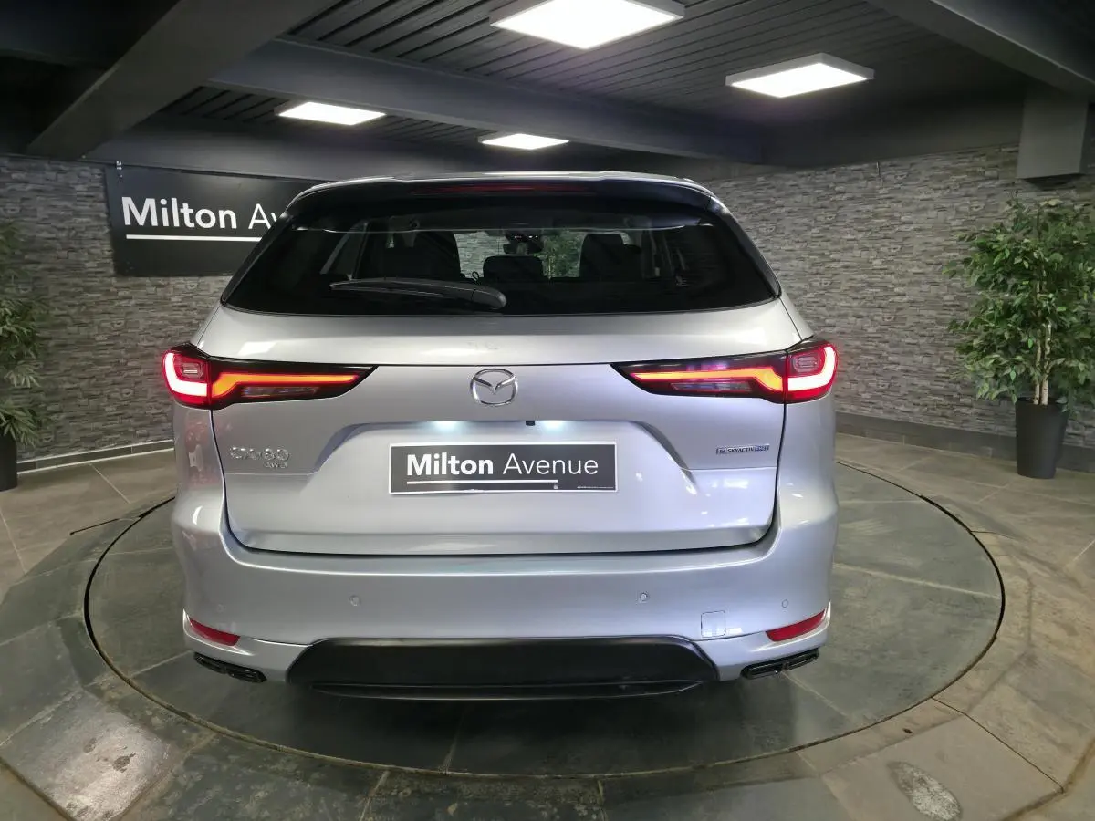 Vue arrière d'un Mazda CX-60 gris Sonic Silver 2023 avec feux LED et logo Mazda visible en intérieur showroom.