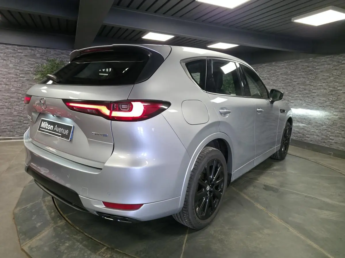 Vue 3/4 arrière droite du Mazda CX-60 gris Sonic Silver avec jantes noires et feux arrière LED allumés.