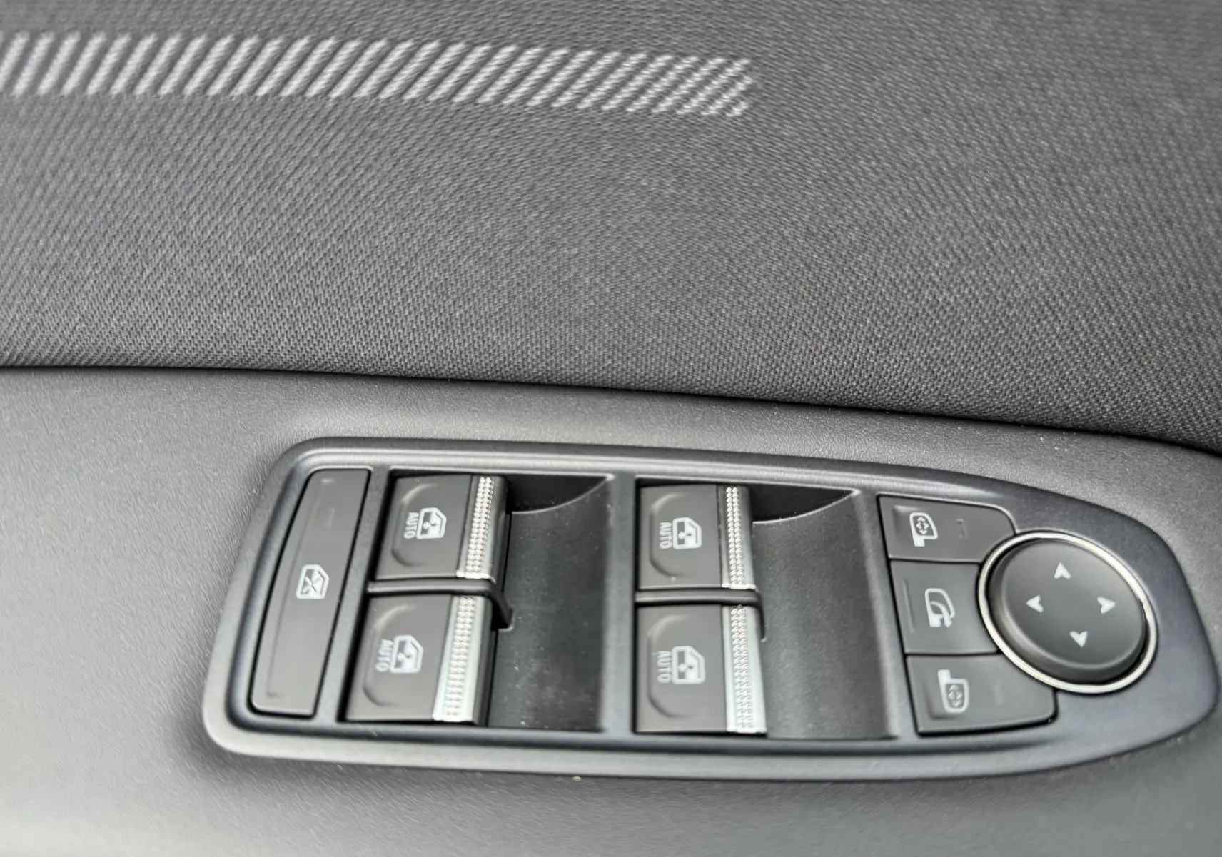 Gros plan sur les commandes des vitres électriques et rétroviseurs côté gauche d'une Renault Symbioz gris cassiopée métal.
