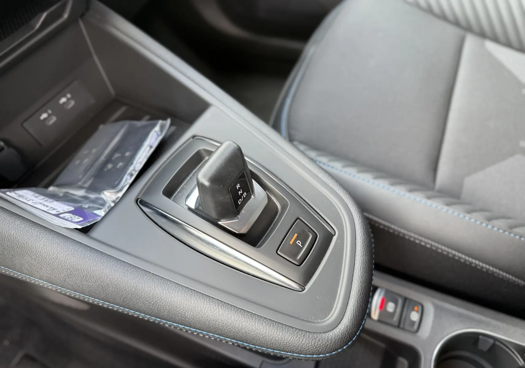 Gros plan sur le levier de vitesses automatique et le bouton parking, avec surpiqûres bleues sur la console intérieure grise.