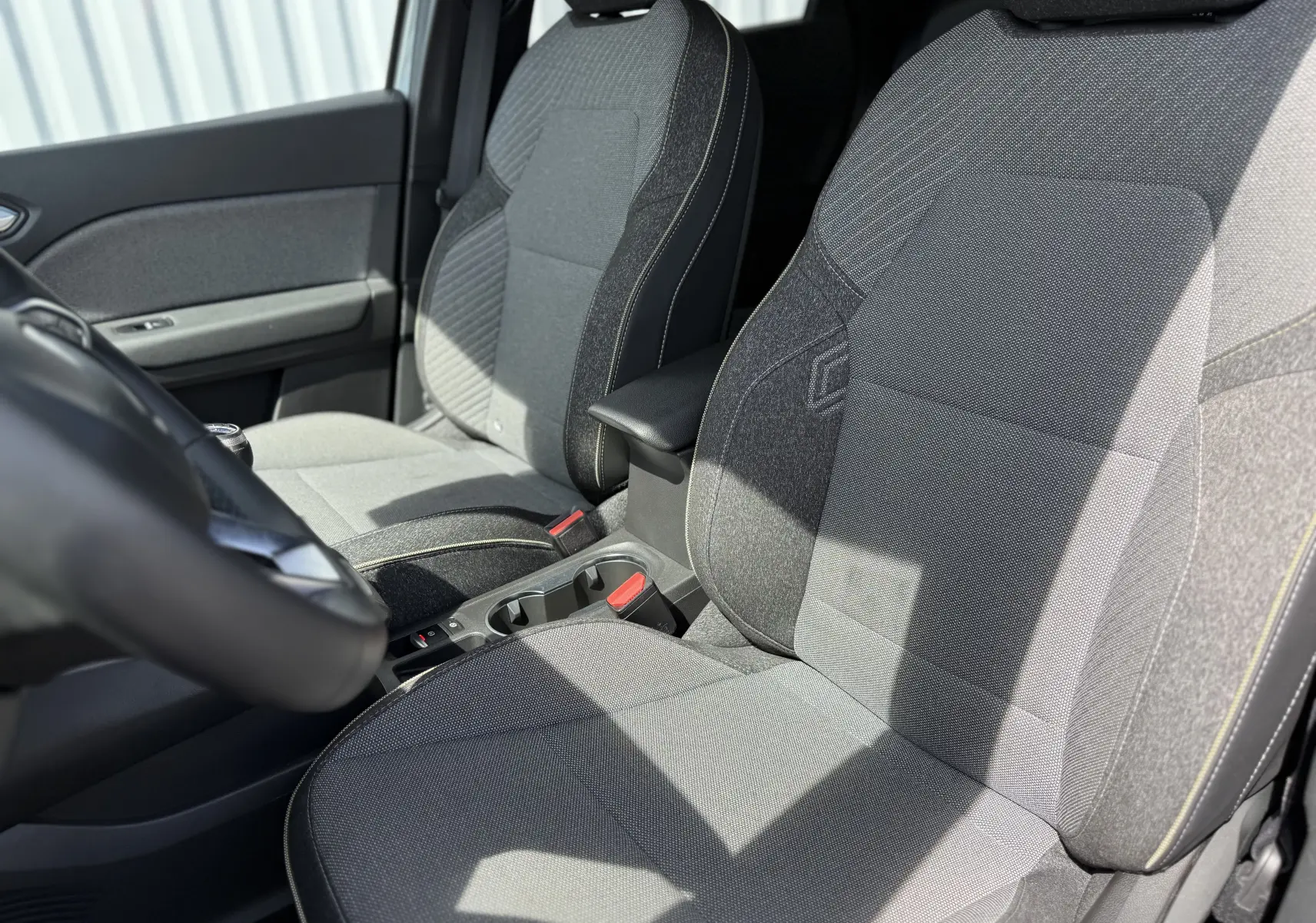 Vue rapprochée des sièges avant gris du Renault Captur 2025, avec accoudoir central et détails de couture visibles.