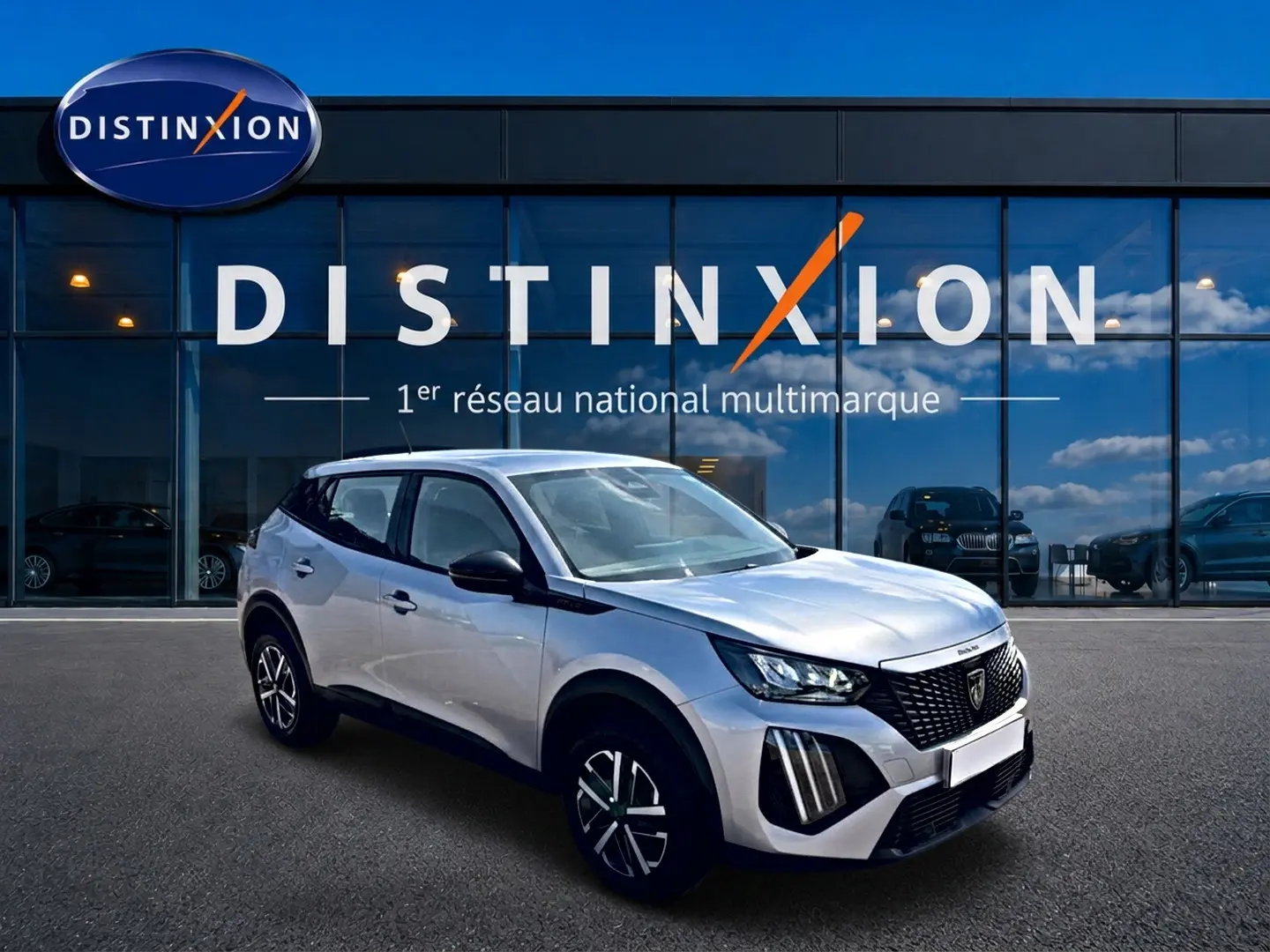 Peugeot 2008 gris en 3/4 avant droit, avec calandre noire et jantes distinctives, devant showroom Distinxion.