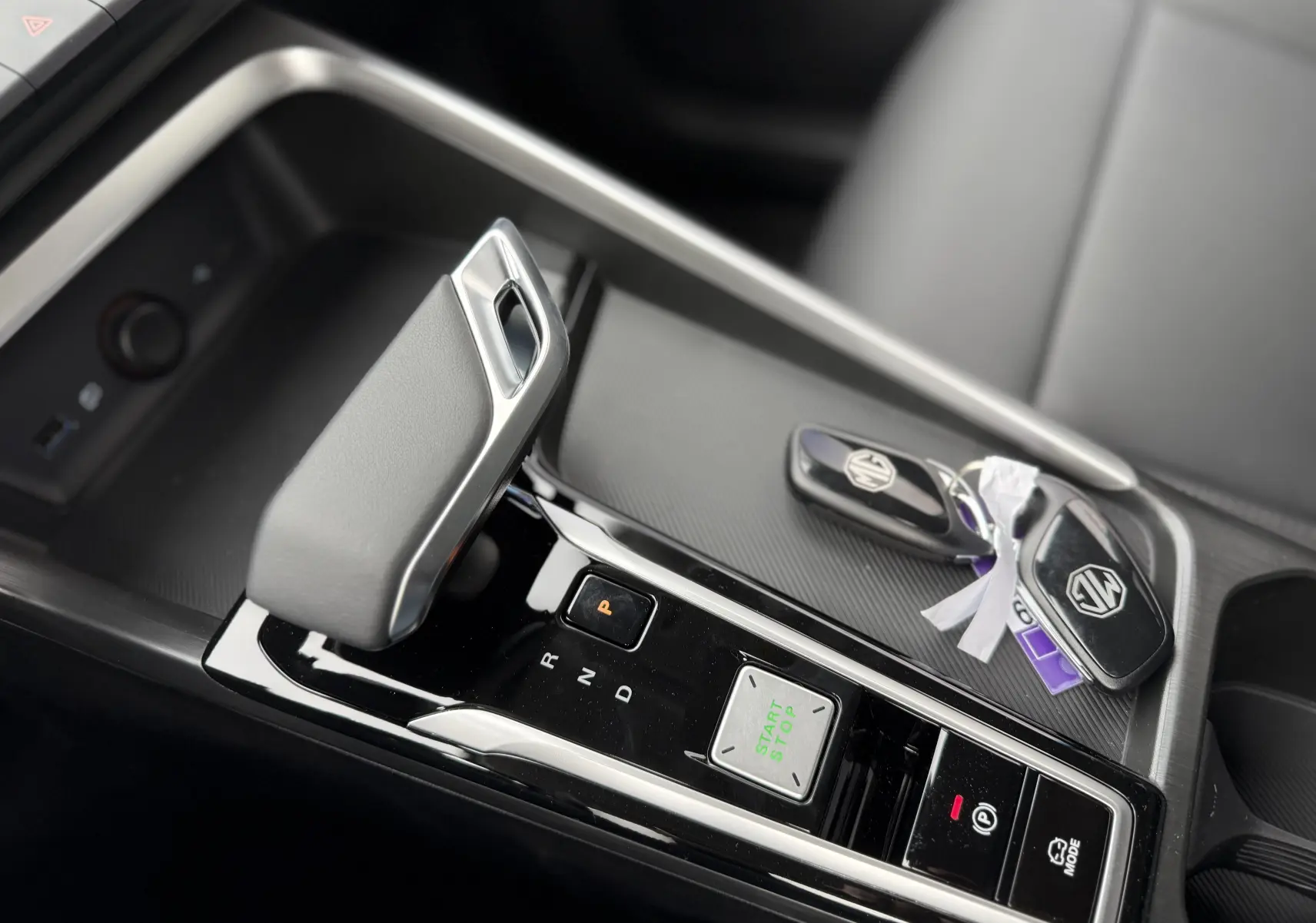 Gros plan sur la console centrale noire du MG Motor ZS 1.5 Hybrid+ avec levier de vitesses et clés à logo MG.