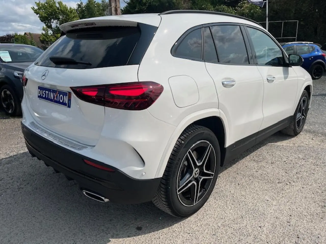 Vue 3/4 arrière droite d'un Mercedes GLA 250 e blanc avec jantes AMG noires et feux arrière LED distinctifs.