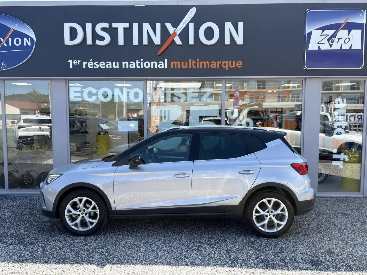Vue profil côté gauche du SEAT Arona 2024 rouge passion avec jantes alliage 16 pouces devant un showroom Distinxion.